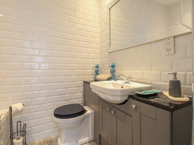 A bathroom with a toilet a sink with grey cabinets and seahorse decorations at The Cottage in Weymouth