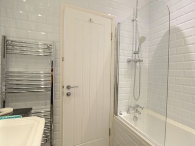 A bathroom with a white door a bathtub with a shower and a heated towel rail at The Cottage in Weymouth