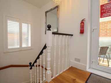 A staircase landing with white balusters and black handrails a window with shutters a fire extinguisher mounted on the wall and a glass door leading outside at The Cottage in Weymouth
