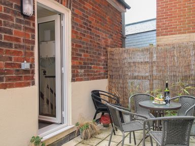 A small outdoor patio with a round table and four chairs next to a brick wall with an open door at The Cottage in Weymouth