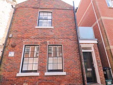 Exterior view of a brick building with three windows and a black door at The Cottage in Weymouth