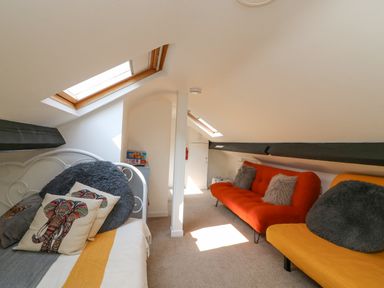 A loft room with a white metal bed with pillows and two sofas under skylights at The Cottage in Weymouth