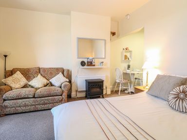 A room with a bed a patterned sofa a small dining table and a stove at The Studio in Sheringham