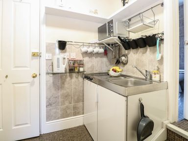 A small kitchen area with a sink stove microwave kettle and hanging kitchen utensils at The Studio in Sheringham