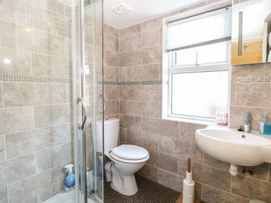 A bathroom with a shower enclosure toilet sink and window at The Studio in Sheringham