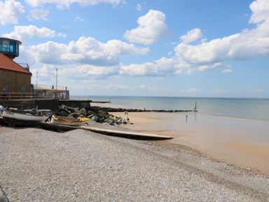 A beach with boats on a pebble shore and a building with a red roof near the water at The Studio in Sheringham