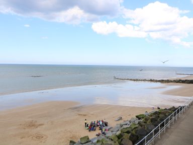 A group of people sitting on the beach near rocks and the sea at The Studio in Sheringham