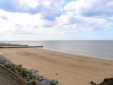 A sandy beach with rock barriers and wooden groynes extending into the sea under a partly cloudy sky at The Studio in Sheringham