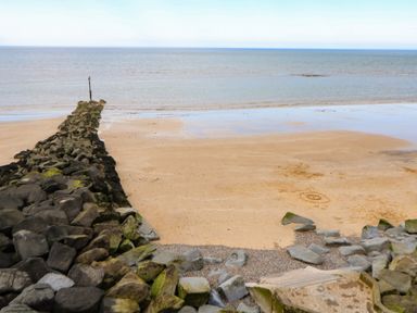 A sandy beach with a rocky breakwater extending into the sea at The Studio in Sheringham