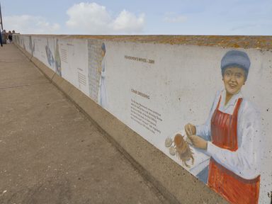 A painted mural on a sea wall depicting fishermen and their wives with accompanying text at The Studio in Sheringham