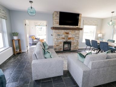 A living room with gray sofas facing a stone fireplace with a mounted TV and a dining table with blue chairs at The Haven in Falcarragh County Donegal