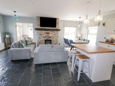 An open living room and kitchen with stone fireplace and gray sofas at The Haven in Falcarragh County Donegal