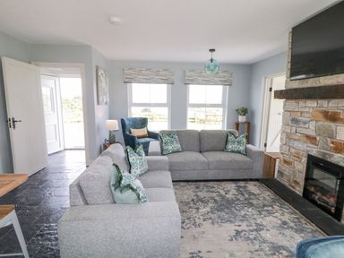 A living room with two gray sofas a blue armchair a stone fireplace and a television at The Haven in Falcarragh County Donegal