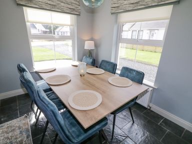A dining area with a wooden table and six blue chairs near two windows at The Haven in Falcarragh County Donegal