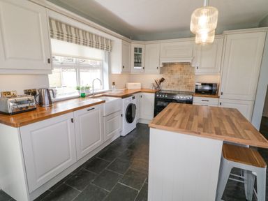 A kitchen with white cabinets wooden countertops a black stove a washing machine a toaster a kettle a microwave and an island with stools at The Haven in Falcarragh County Donegal