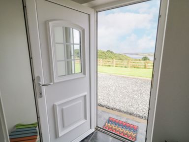 An open white door showing a doormat outside a gravel path with a wooden fence and grassy area beyond at The Haven in Falcarragh County Donegal