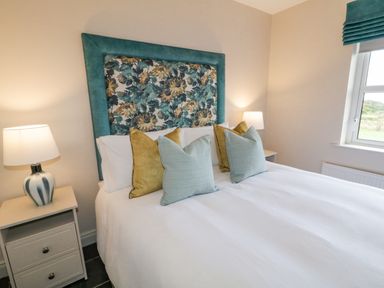 A bedroom with a bed with a floral headboard and pillows bedside tables with lamps and a window at The Haven in Falcarragh County Donegal
