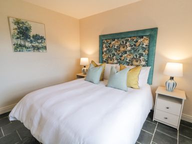 A bedroom with a double bed white bedding floral upholstered headboard two bedside tables with lamps and a painting on the wall at The Haven in Falcarragh County Donegal
