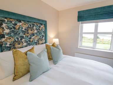 A bedroom with a bed with patterned headboard and four pillows near a window with a blue blind at The Haven in Falcarragh County Donegal