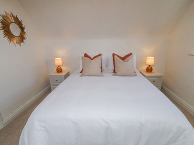 A bedroom with a double bed white bedding and four pillows two bedside tables with lamps and a decorative wall mirror at The Haven in Falcarragh County Donegal