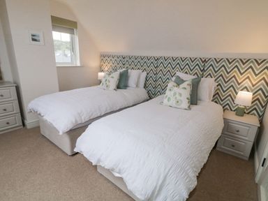 A bedroom with two single beds with white bedding green and patterned cushions chevron headboard bedside tables and lamps at The Haven in Falcarragh County Donegal