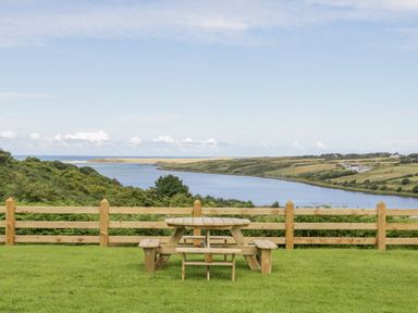 A picnic table on grass with a wooden fence and water and hills in the background at The Haven in Falcarragh County Donegal