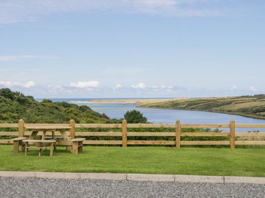 A wooden picnic table on grass near a wooden fence overlooking a river and fields at The Haven in Falcarragh County Donegal