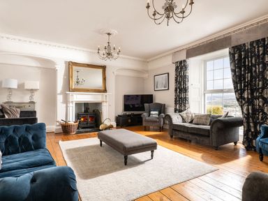 A living room with a fireplace a large window a gray sofa a blue sofa and a gray ottoman at Fron Dderw Bala