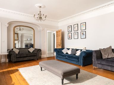 A living room with three sofas a large mirror a chandelier six framed pictures on the wall and a rectangular ottoman at Fron Dderw in Bala