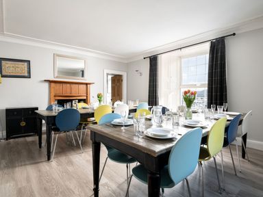 A dining room with two wooden tables set with plates glasses and flowers at Fron Dderw in Bala