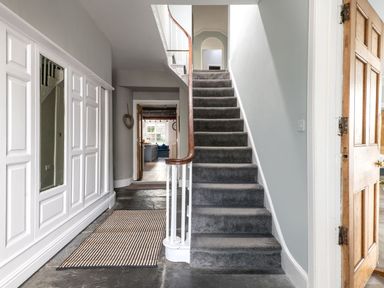A hallway with carpeted stairs and a striped rug on stone floor at Fron Dderw in Bala