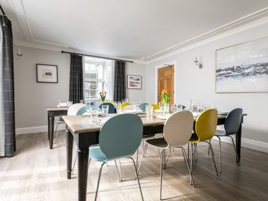 A dining room with a wooden table and colorful chairs and flowers on the table at Fron Dderw in Bala