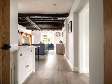 A kitchen with wooden beams on the ceiling a blue island a window seat and white cabinets at Fron Dderw in Bala