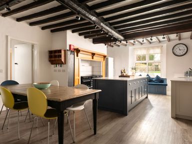 A kitchen with a dining table and chairs a kitchen island a window seat and a clock on the wall at Fron Dderw in Bala