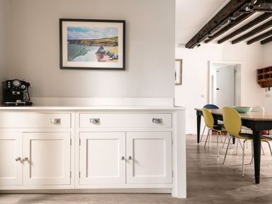 A kitchen counter with a coffee machine and a framed painting above next to a dining table with colorful chairs at Fron Dderw in Bala