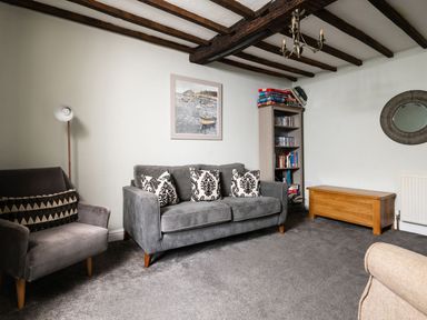 A living room with a grey sofa and armchair a bookshelf a wooden chest and a round mirror at Fron Dderw in Bala