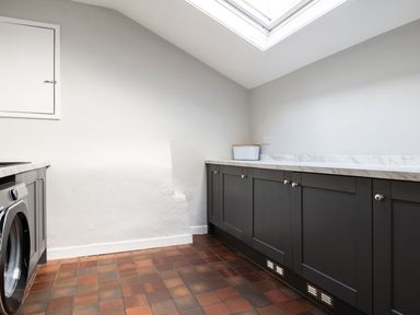 A laundry room with dark cabinets a washing machine a tiled floor and a skylight window at Fron Dderw in Bala
