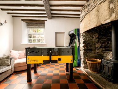 A room with a foosball table arcade machine sofas a stone fireplace and basket at Fron Dderw in Bala