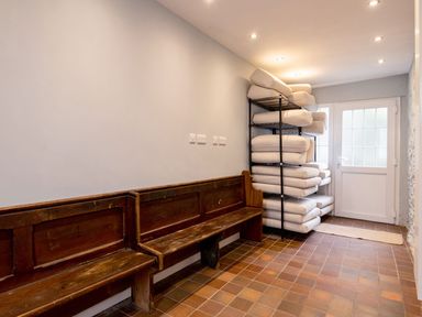 A room with wooden benches against a wall and a metal rack holding stacked cushions near a door at Fron Dderw in Bala