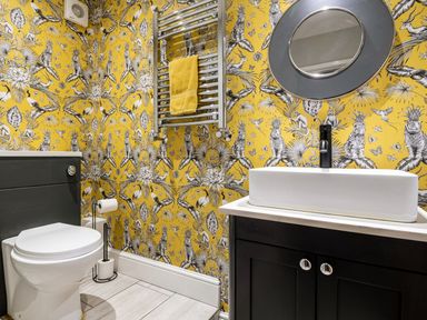 A bathroom with a toilet a black vanity with a white sink a round mirror and a heated towel rail with a yellow towel at Fron Dderw in Bala