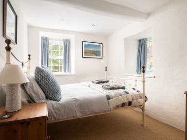 A bedroom with a metal bed frame and two windows with blue curtains at Fron Dderw in Bala