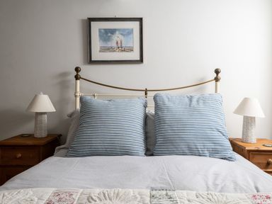 A bedroom with a bed with two blue striped pillows two wooden bedside tables with lamps and a painting above the bed at Fron Dderw in Bala