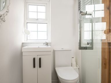 A bathroom with a white sink cabinet a toilet a window and a glass shower door at Fron Dderw in Bala
