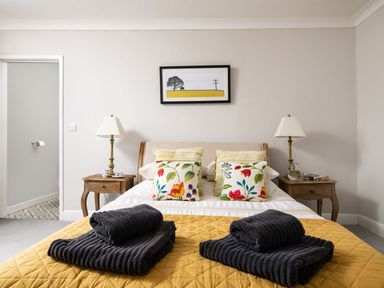 A bedroom with a bed featuring floral cushions and folded towels on a yellow quilt at Fron Dderw in Bala