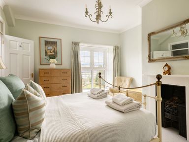 A bedroom with a bed folded towels and pillows a chest of drawers an armchair a fireplace a mirror and a window at Fron Dderw in Bala