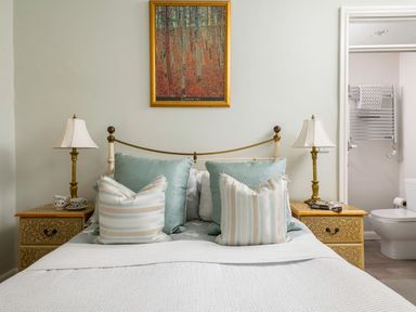 A bedroom with a bed with pillows two bedside tables with lamps and a doorway to a bathroom at Fron Dderw in Bala