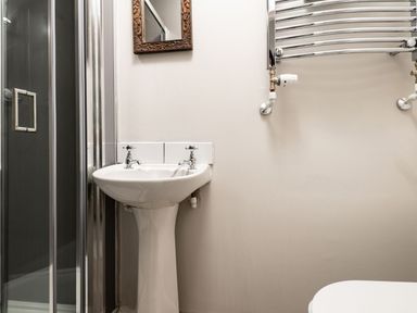 A bathroom with a pedestal sink, a wall-mounted mirror, a towel radiator, and a glass shower enclosure at Fron Dderw in Bala