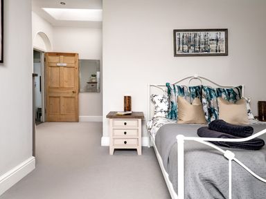 A bedroom with a white metal bed frame pillows and a bedside table next to a wooden door with a mirror on the wall at Fron Dderw in Bala