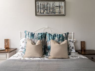 A bed with patterned pillows and a gray blanket with wooden bedside tables and lamps at Fron Dderw in Bala