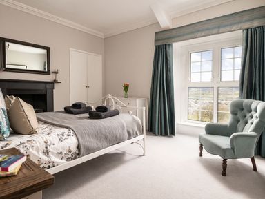 A bedroom with a bed, armchair, window with curtains, dresser, mirror, and fireplace at Fron Dderw in Bala